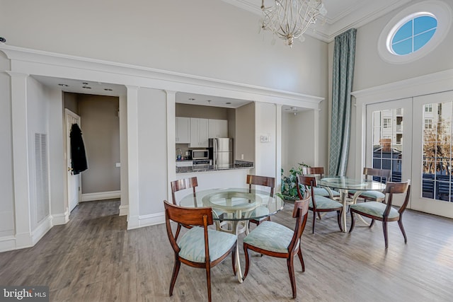 dining area featuring ornate columns, a towering ceiling, crown molding, light wood-type flooring, and french doors