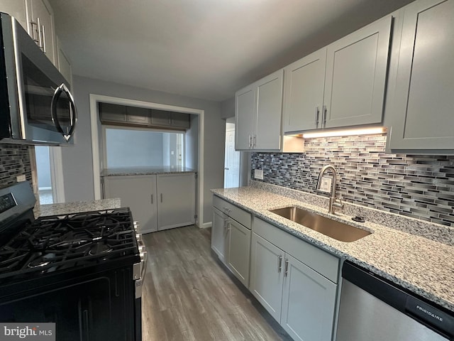 kitchen featuring appliances with stainless steel finishes, sink, decorative backsplash, light hardwood / wood-style floors, and light stone countertops