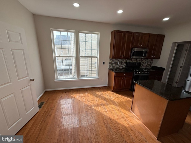 kitchen featuring black range with gas stovetop, light hardwood / wood-style floors, backsplash, and a center island