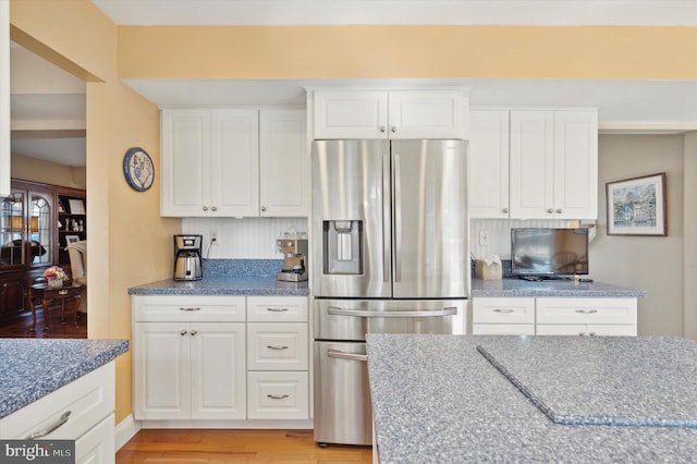 kitchen with light wood-type flooring, light stone countertops, white cabinets, and stainless steel fridge with ice dispenser