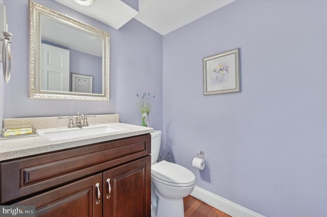 half bath featuring toilet, baseboards, wood finished floors, and vanity