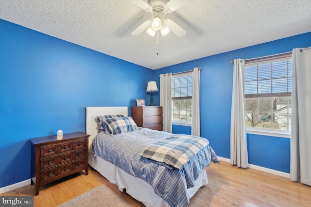 bedroom featuring a ceiling fan, light wood-type flooring, a textured ceiling, and baseboards