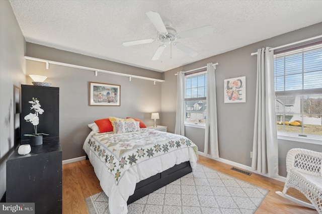 bedroom with baseboards, visible vents, a textured ceiling, and light wood finished floors