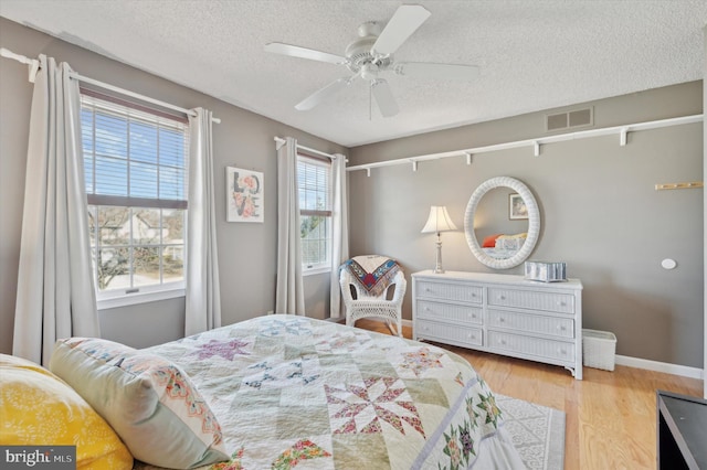 bedroom featuring light wood finished floors, baseboards, visible vents, a ceiling fan, and a textured ceiling