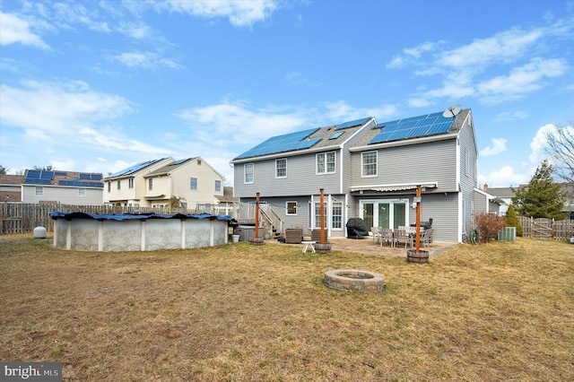 rear view of house featuring an outdoor fire pit, fence, roof mounted solar panels, and an outdoor pool