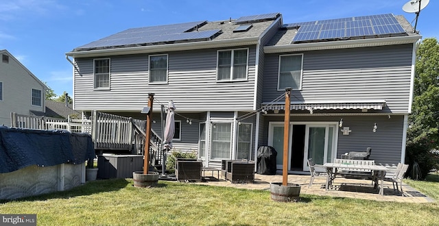 rear view of house with a patio, a wooden deck, a lawn, and solar panels