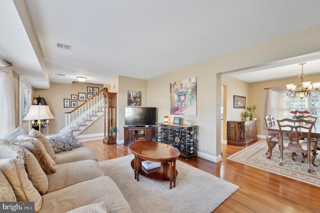 living room featuring a chandelier, wood finished floors, visible vents, and stairs