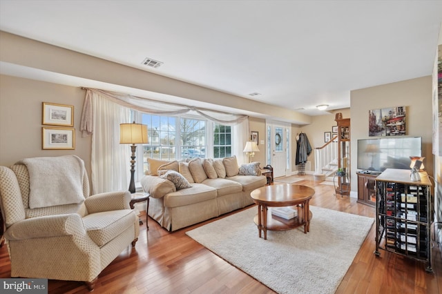 living room featuring visible vents, stairway, baseboards, and wood finished floors