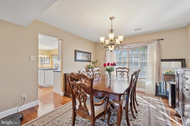 dining space with an inviting chandelier, light wood-style flooring, visible vents, and baseboards