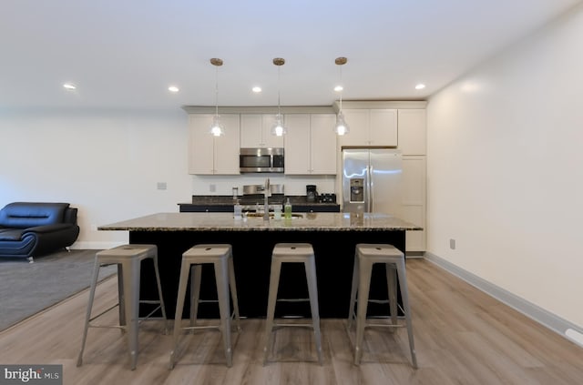 kitchen with sink, appliances with stainless steel finishes, white cabinets, a center island with sink, and dark stone counters