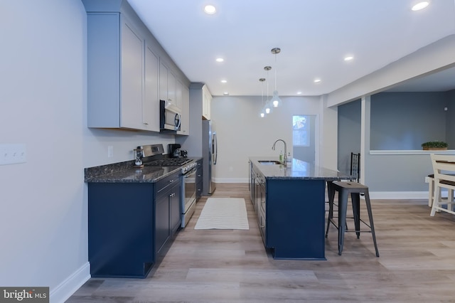 kitchen featuring pendant lighting, stainless steel appliances, a center island with sink, and dark stone countertops