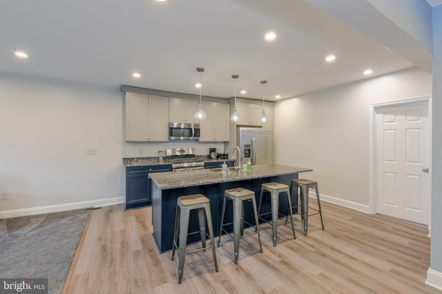 kitchen featuring a breakfast bar area, decorative light fixtures, dark stone countertops, an island with sink, and stainless steel appliances