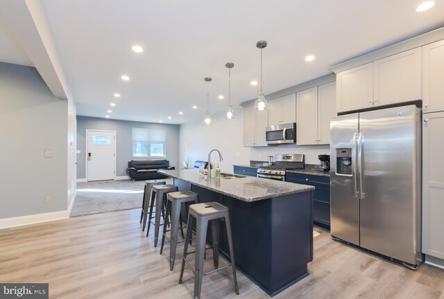 kitchen with decorative light fixtures, sink, dark stone countertops, a kitchen island with sink, and stainless steel appliances