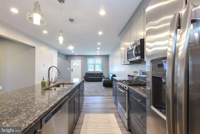 kitchen with appliances with stainless steel finishes, decorative light fixtures, sink, dark stone countertops, and dark hardwood / wood-style flooring