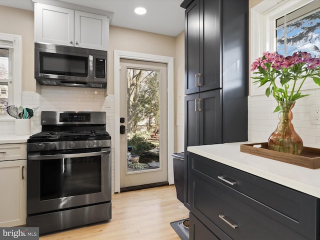 kitchen with backsplash, stainless steel appliances, light wood-type flooring, and white cabinets