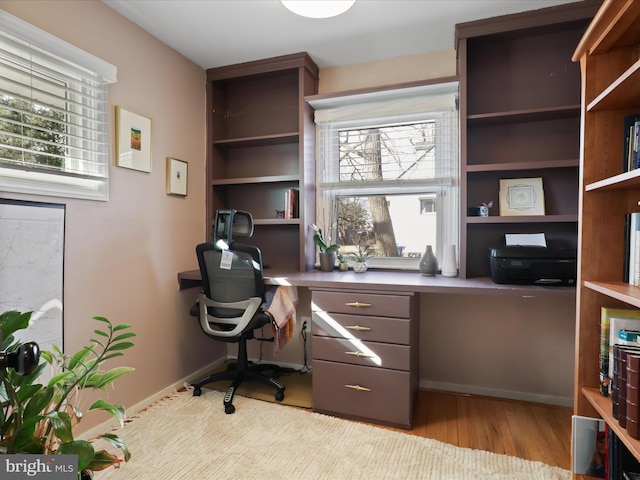 office area with plenty of natural light, built in desk, and light hardwood / wood-style floors