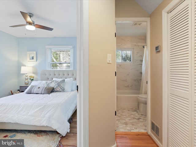 bedroom with multiple windows, ensuite bath, ceiling fan, and light wood-type flooring