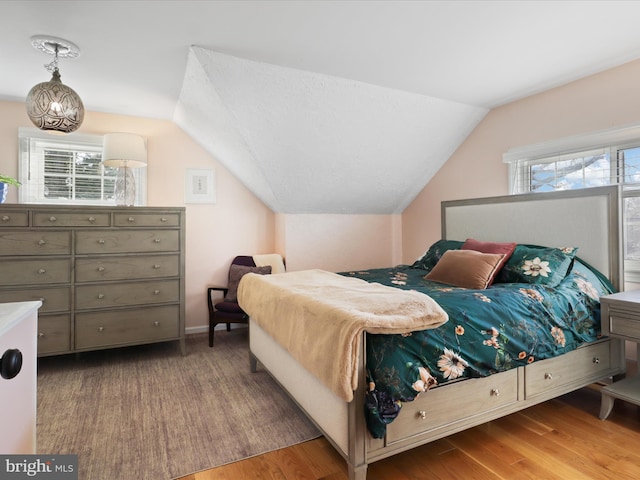 bedroom with wood-type flooring, vaulted ceiling, and multiple windows