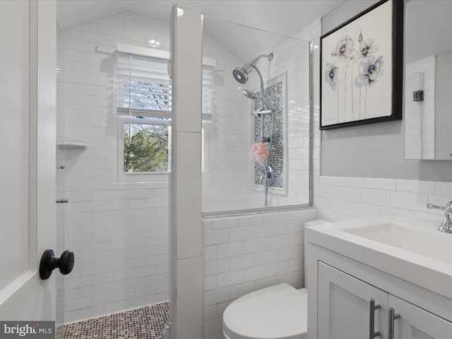 bathroom featuring vaulted ceiling, a tile shower, tile walls, vanity, and toilet