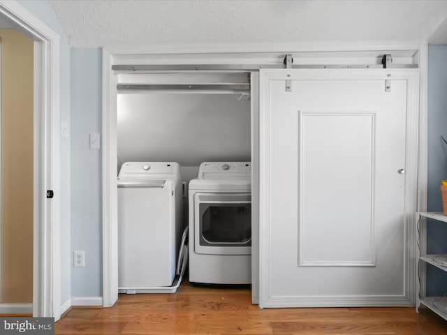 clothes washing area with light hardwood / wood-style floors, washer and dryer, and a textured ceiling