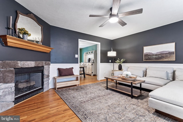 living room featuring ceiling fan, wood-type flooring, a fireplace, and a textured ceiling