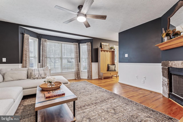 living room featuring hardwood / wood-style flooring, ceiling fan, a fireplace, and a textured ceiling