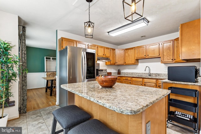 kitchen with light tile patterned floors, sink, appliances with stainless steel finishes, hanging light fixtures, and a center island