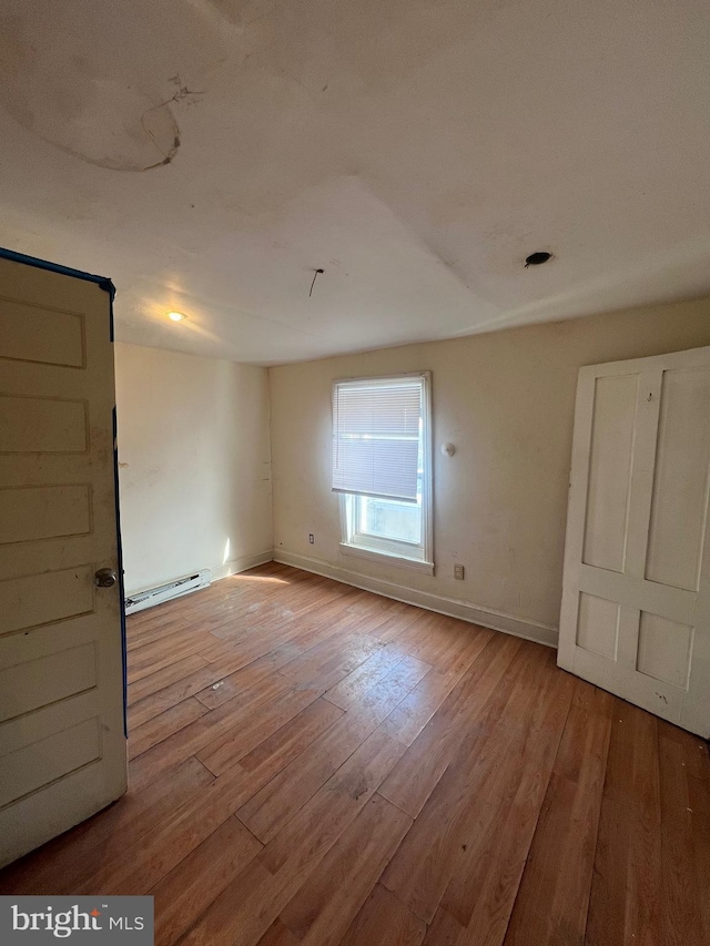 unfurnished room with baseboard heating and light hardwood / wood-style floors