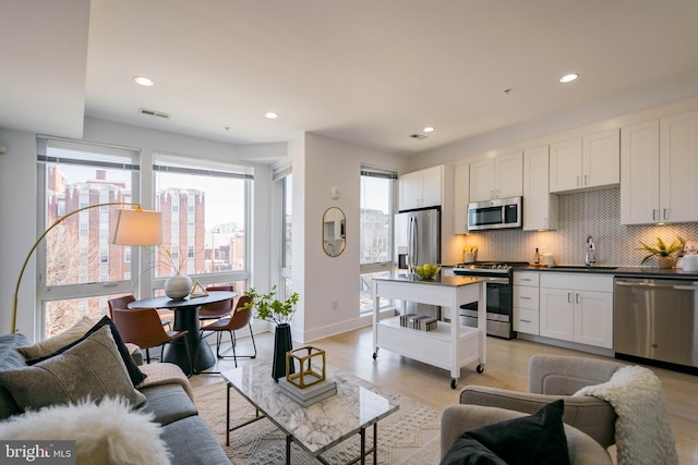 kitchen featuring sink, white cabinetry, stainless steel appliances, light hardwood / wood-style floors, and decorative backsplash