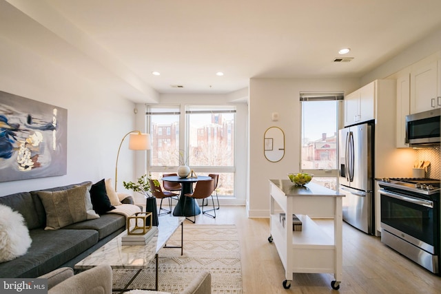 kitchen featuring white cabinetry, decorative backsplash, stainless steel appliances, and light hardwood / wood-style floors