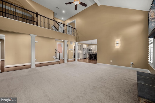 unfurnished living room featuring high vaulted ceiling, decorative columns, beamed ceiling, carpet flooring, and ceiling fan