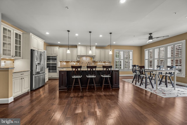 kitchen with pendant lighting, a kitchen bar, a center island, stainless steel appliances, and light stone countertops