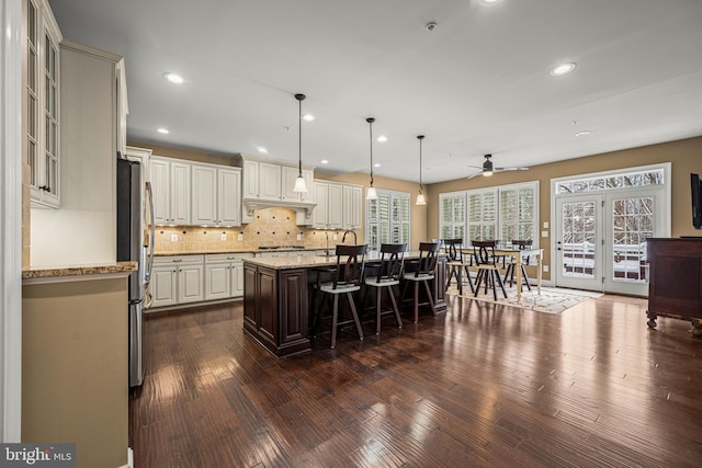 kitchen featuring a kitchen bar, stainless steel refrigerator, pendant lighting, light stone countertops, and a kitchen island with sink