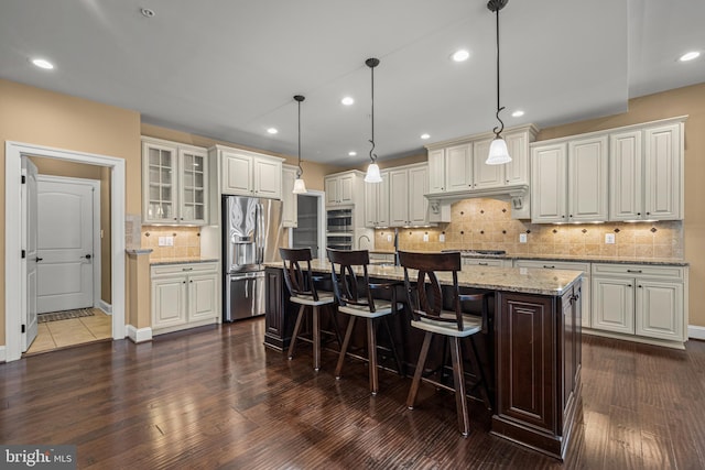 kitchen featuring a kitchen bar, hanging light fixtures, a kitchen island with sink, light stone counters, and stainless steel appliances