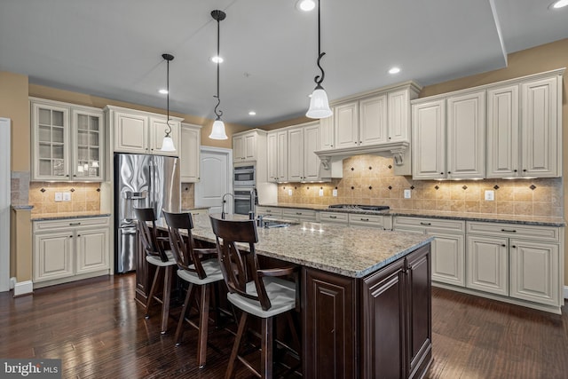 kitchen with hanging light fixtures, appliances with stainless steel finishes, a center island with sink, and white cabinets