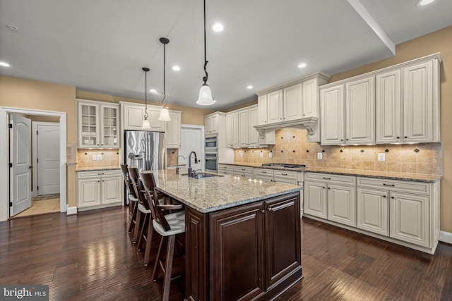 kitchen featuring a kitchen bar, dark hardwood / wood-style flooring, pendant lighting, stainless steel appliances, and a kitchen island with sink