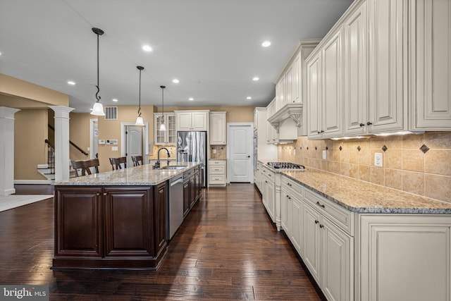 kitchen featuring a large island, appliances with stainless steel finishes, hanging light fixtures, light stone counters, and ornate columns