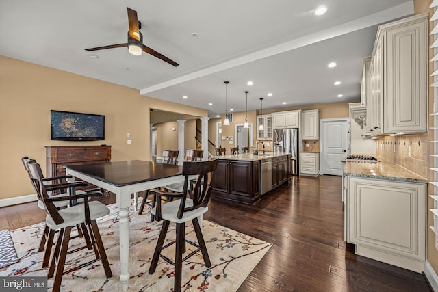 dining space featuring dark hardwood / wood-style flooring, sink, decorative columns, and ceiling fan