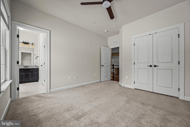 unfurnished bedroom featuring ensuite bathroom, light colored carpet, ceiling fan, and a closet