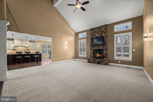 carpeted living room featuring a stone fireplace, high vaulted ceiling, and ceiling fan