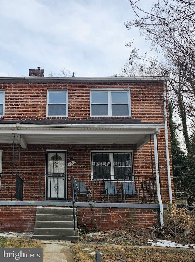 view of front of home featuring a porch, brick siding, and a chimney