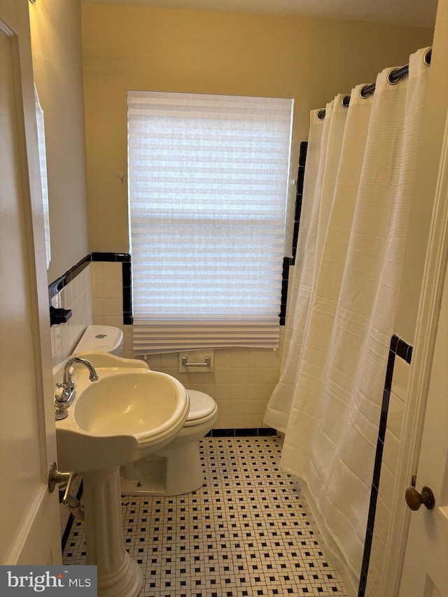 bathroom with toilet, curtained shower, wainscoting, and tile walls