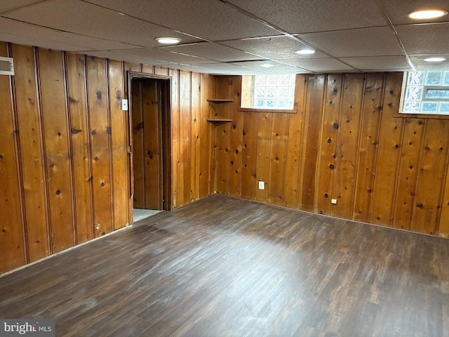 below grade area with a drop ceiling, wood walls, and wood finished floors