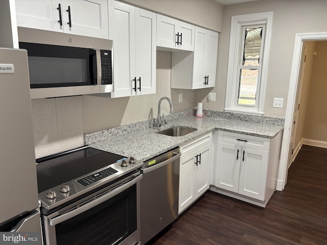 kitchen with white cabinets, light stone counters, appliances with stainless steel finishes, dark wood-type flooring, and a sink