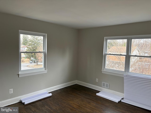 spare room with baseboards, visible vents, and dark wood-style flooring