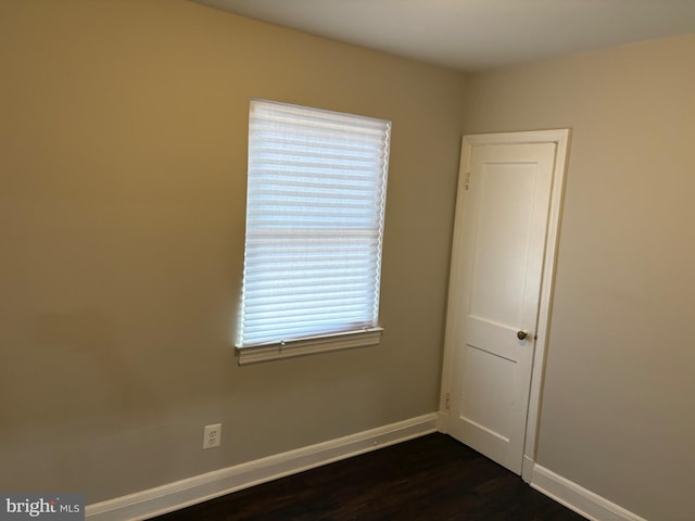 spare room with baseboards and dark wood finished floors