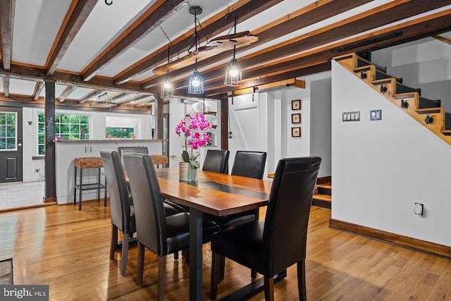 dining space with beam ceiling, a barn door, and light wood-type flooring