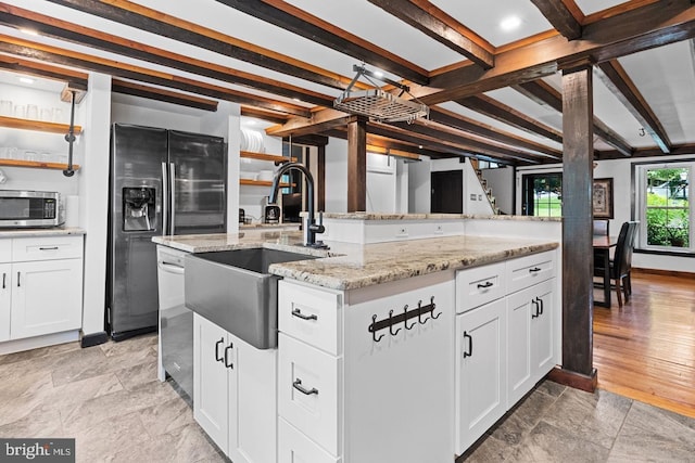 kitchen featuring beamed ceiling, white cabinetry, an island with sink, sink, and stainless steel appliances