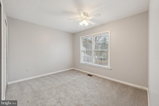 empty room featuring a ceiling fan, light colored carpet, visible vents, and baseboards