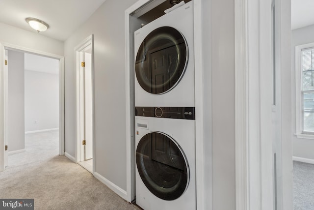 washroom featuring light carpet, laundry area, baseboards, and stacked washer / dryer